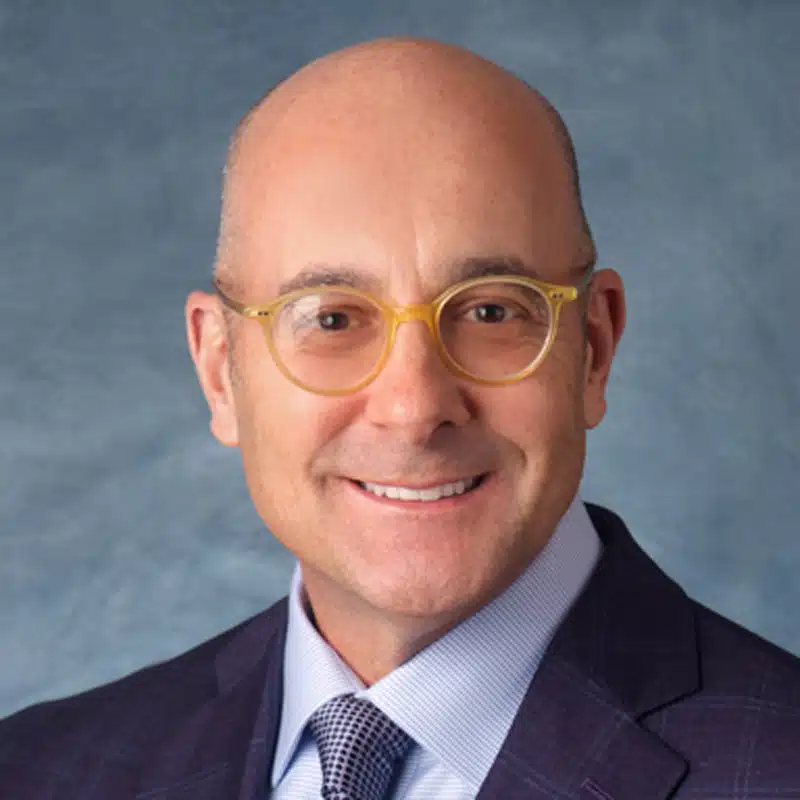 a man wearing a suit and tie smiling at the camera