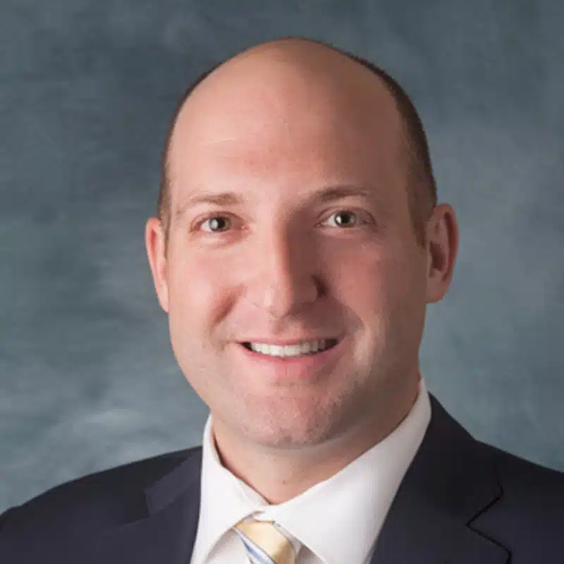 a man wearing a suit and tie smiling at the camera